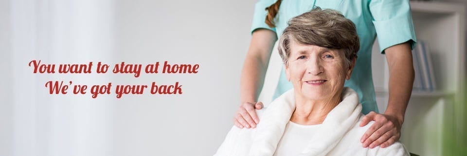 An old woman sits in front of a personal support worker as they both face the camera